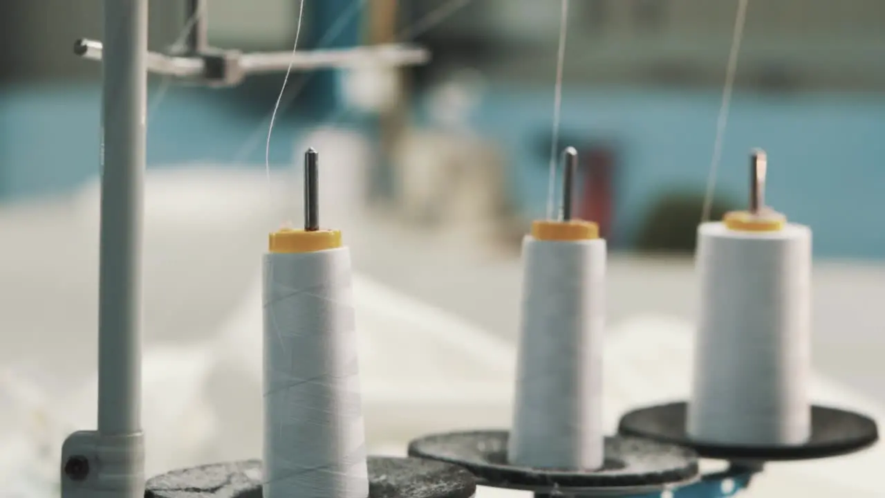 Close-up of white threads on a factory sewing machine on the background of sewn textiles made of white fabric