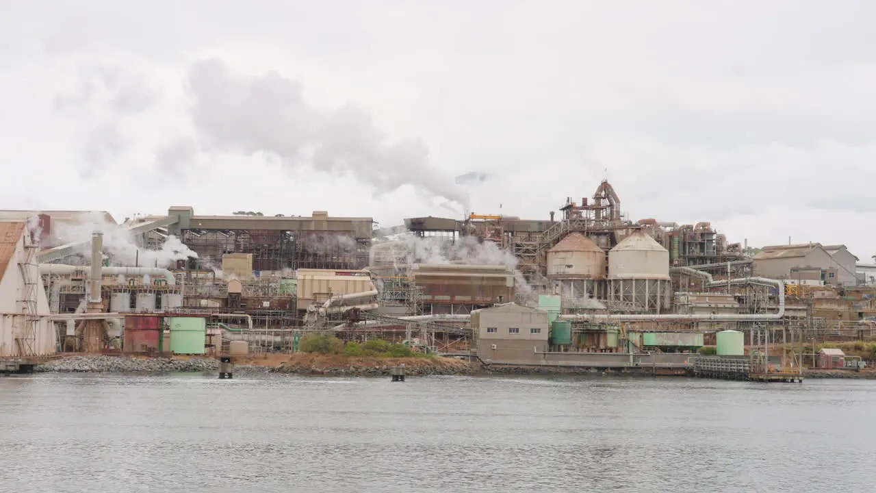 Riverside Steampunk Industrial Factory Area Emitting Smoke From Smokestack 4K Slow Motion