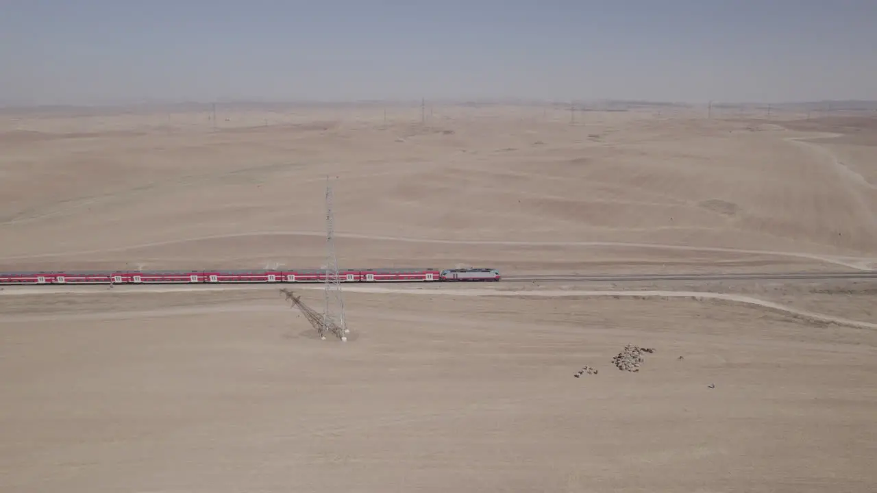 Aerial shot of a red passenger train in a remote and desert area near large electricity poles dry land without crops on the ground there is a female shepherd with sheeps-1