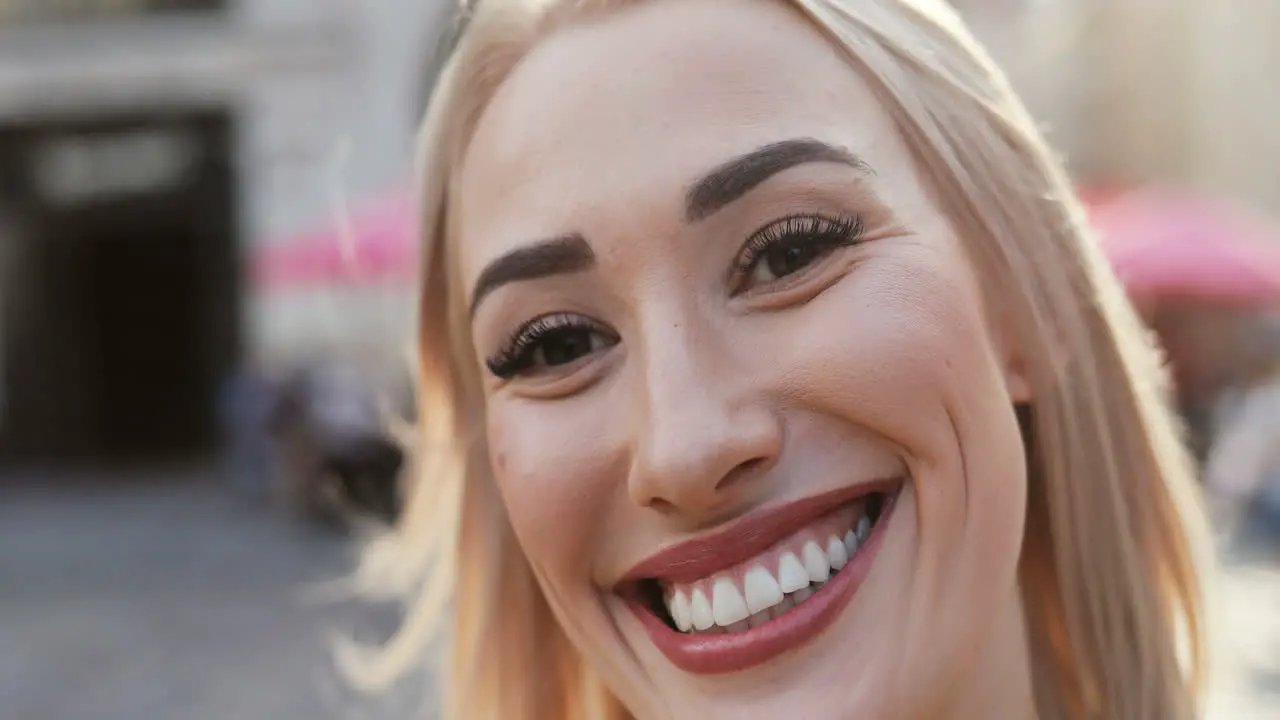 Close Up Of The Smiling Blonde Happy Young Woman Laughing Cheerfully While Looking At The Camera And Her Hair Waving On The Wind