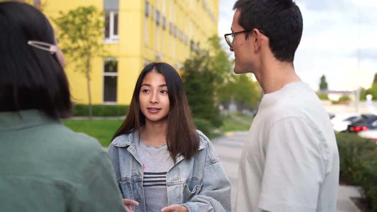 Group Of Three Happy Young Japanese Friends Standing Outdoors And Talking To Each Other 1