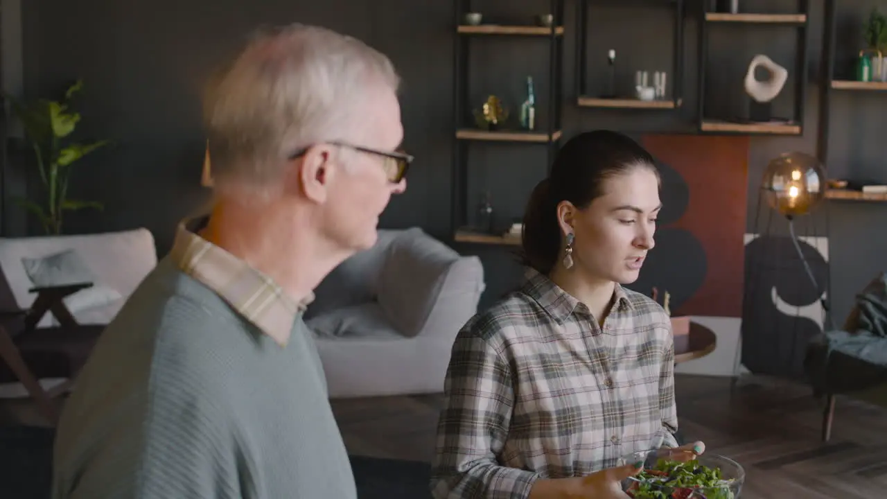 Happy Family Standing Near The Table In Living Room Talking And Having Meal Together