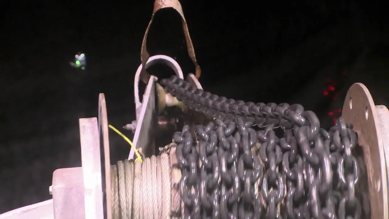 A sea vessel reels in a chain at night