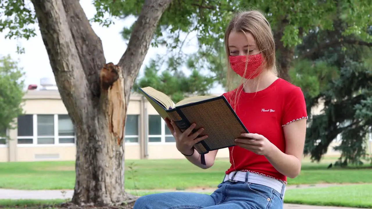 A young student reads while social distancing and wearing a mask on campus