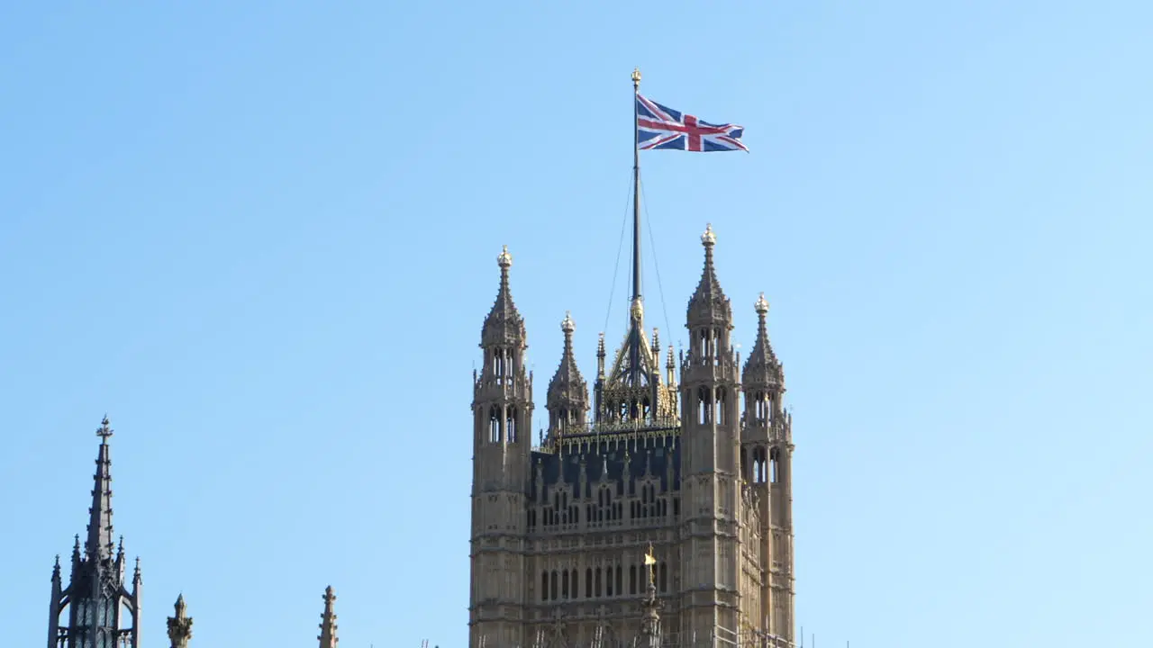 British Union flag in slow motion above famous Victoria Tower blue sky