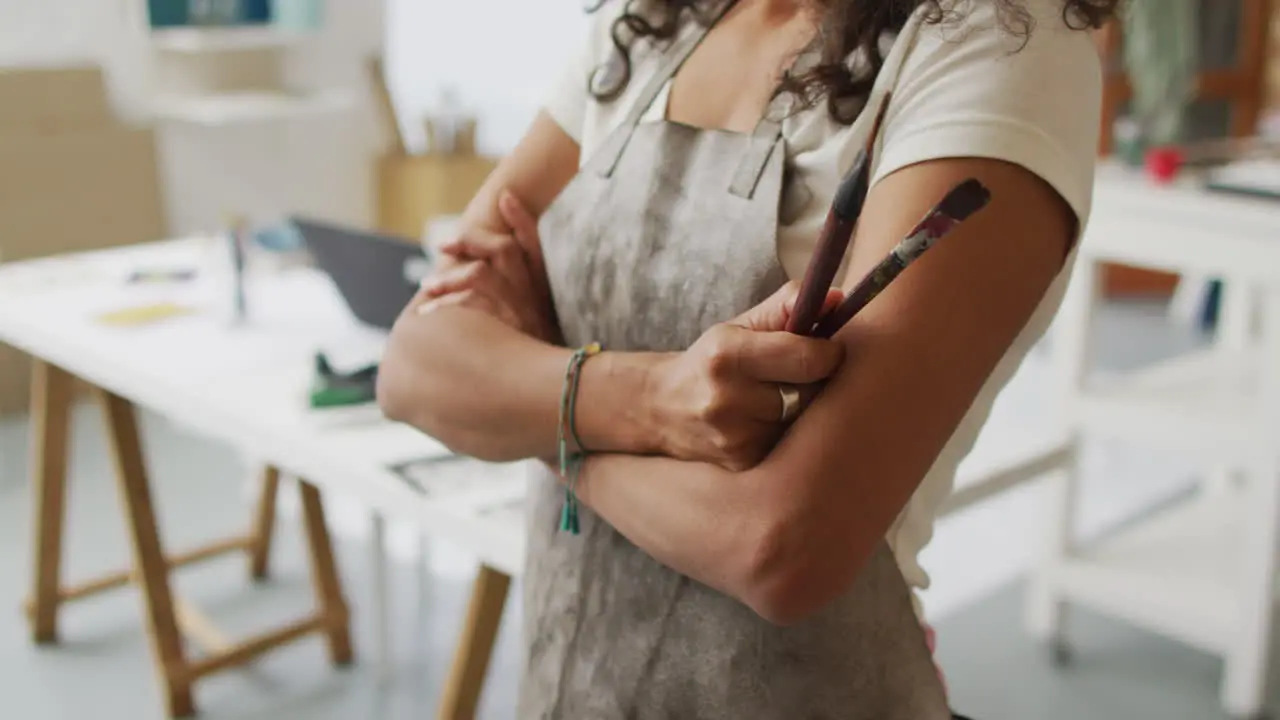 Artist in a studio arms crossed holding a paintbrush