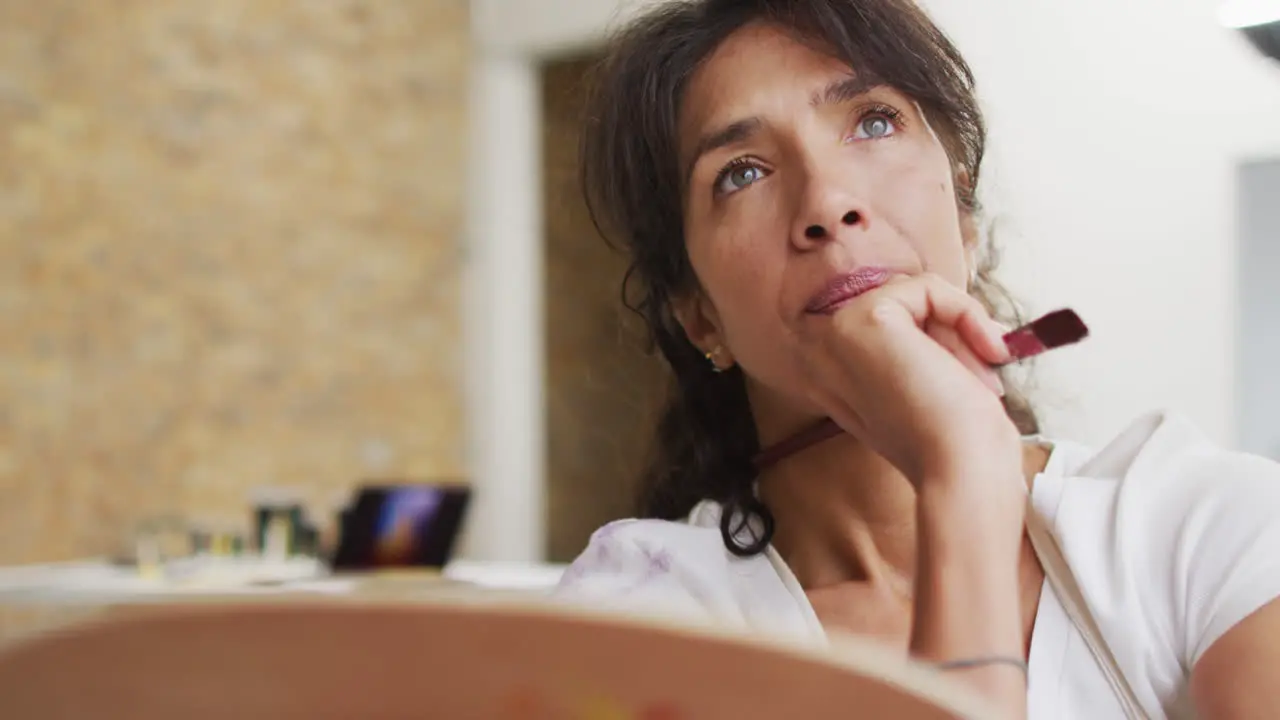 Biracial woman ponders over her painting at home