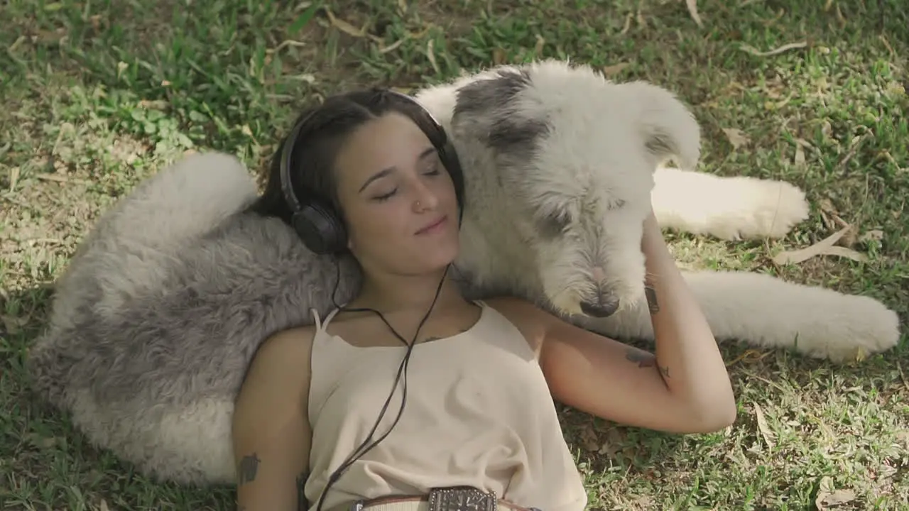 Young Woman With Headphones Pets A Big Dog Lying On The Grass