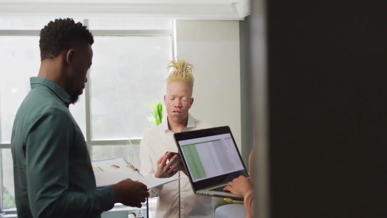 Diverse business people discussing with laptop and documents in creative office