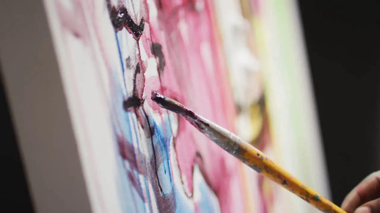 Close up of hand of male artist painting with paint brush on canvas at art studio