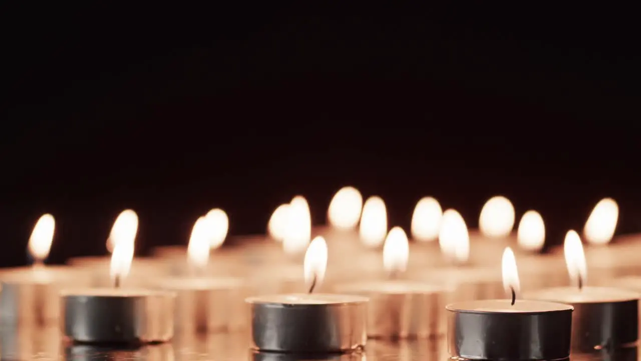 Video of rows of tea candles with white flames and copy space on black background