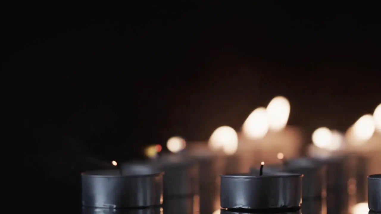 Video of close up of rows of tea candles with white flames and copy space on black background