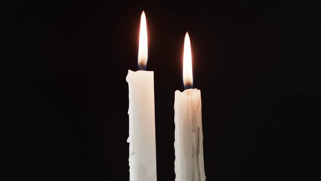 Video of two white candles with white flame and copy space on black background