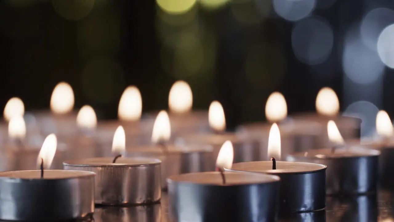 Video of row of tea candles with white flames and copy space with bokeh on black background