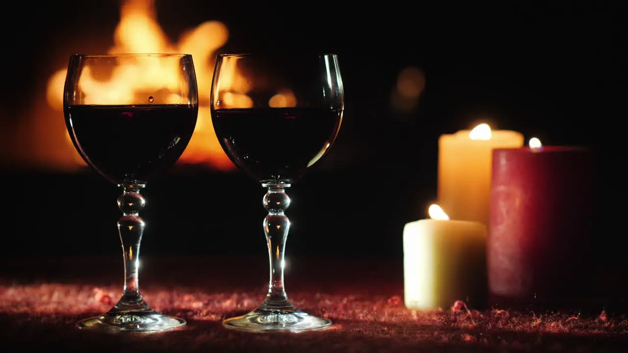 Two Glasses With Red Wine Against The Background Of The Fireplace Where The Fire Is Burning