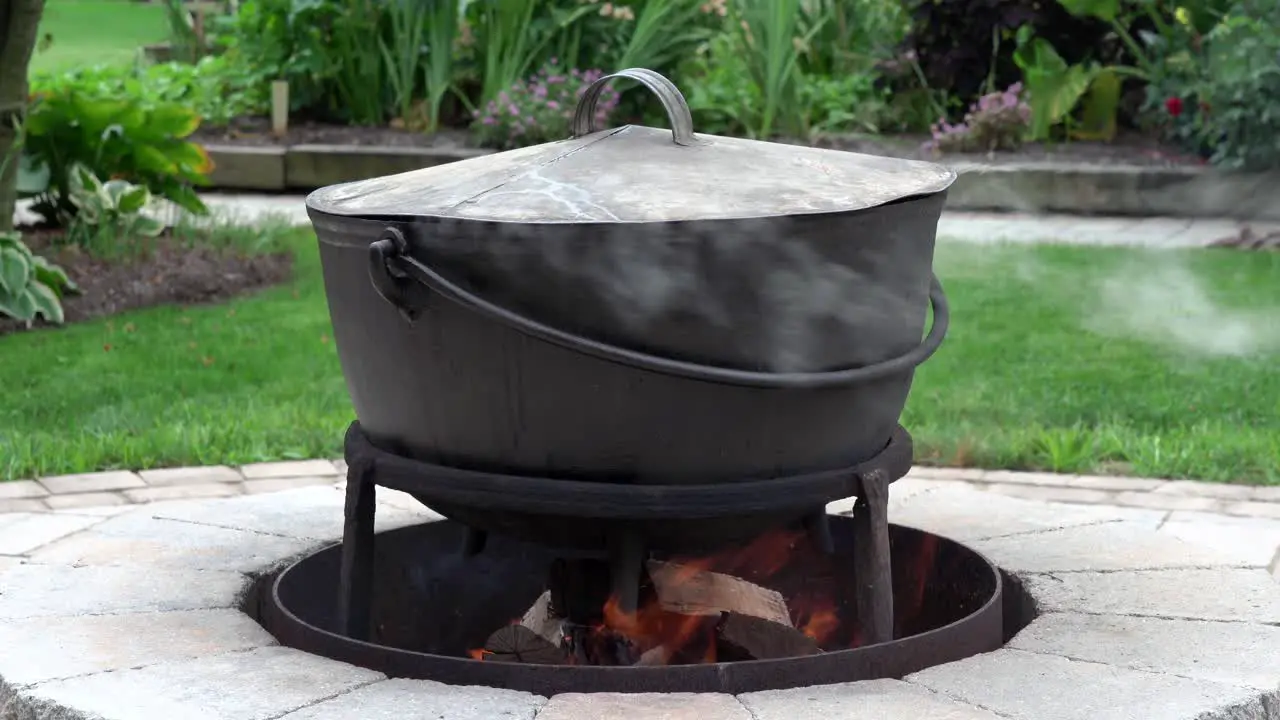 A fire burning in an outdoor fireplace and heating an old iron kettle