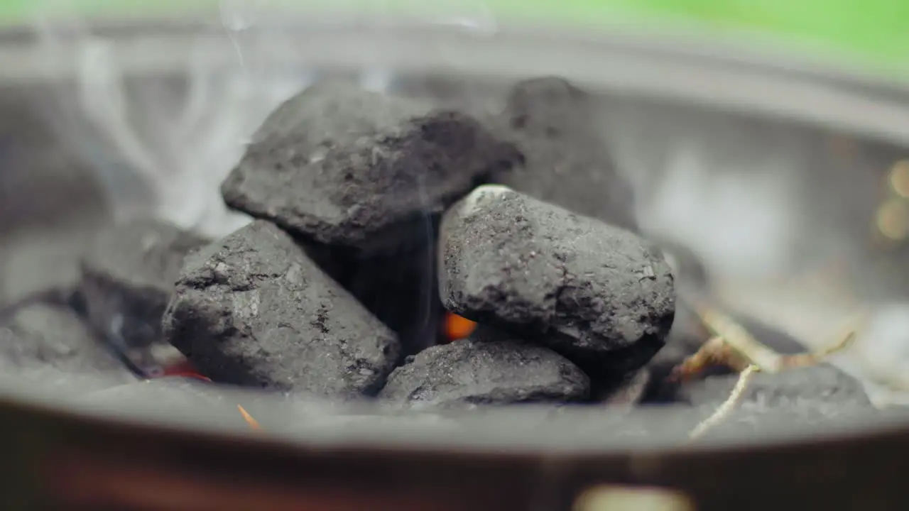 Charcoal laying in a black pan smoking starting to glow on a summer day with blurred grass in the background