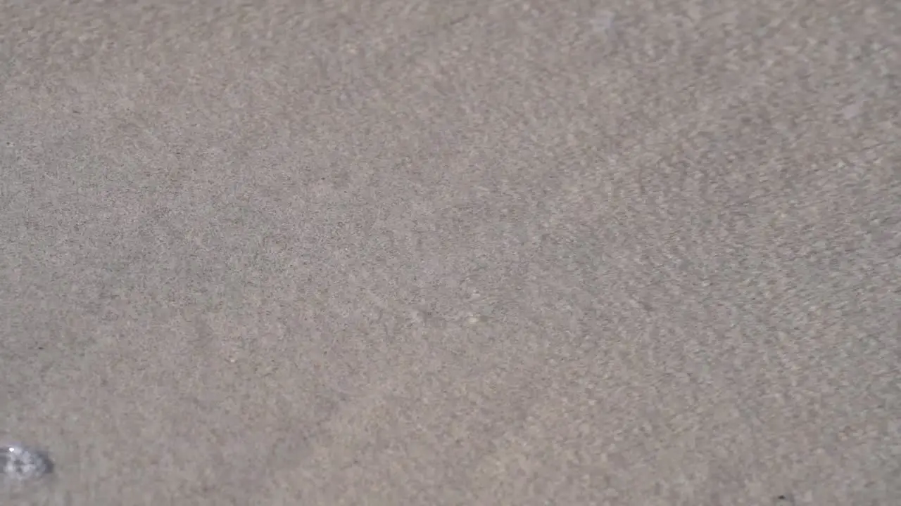 Close-up footage of clear refreshing water washing over white sand