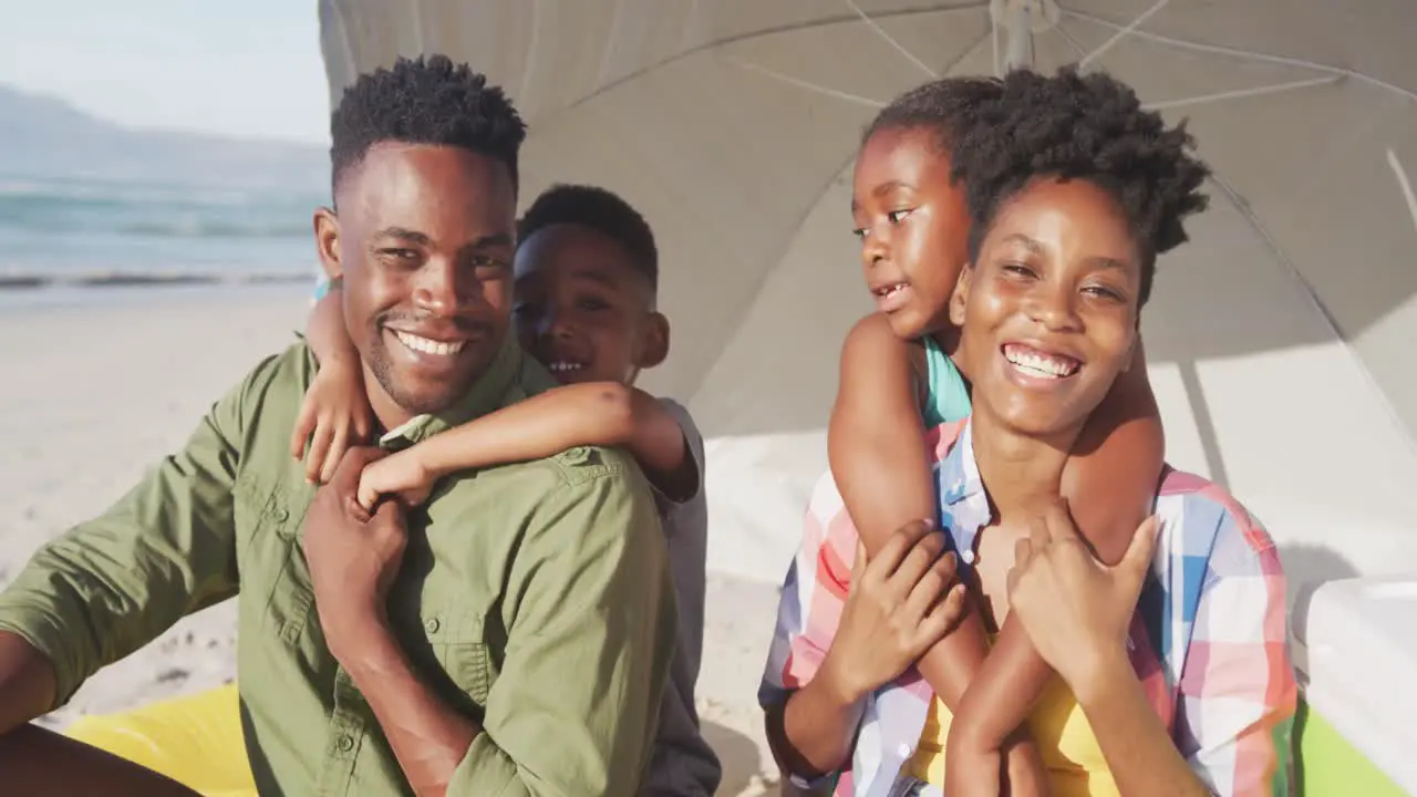 Portrait of african american family smiling while sitting under a umbrella on the beach