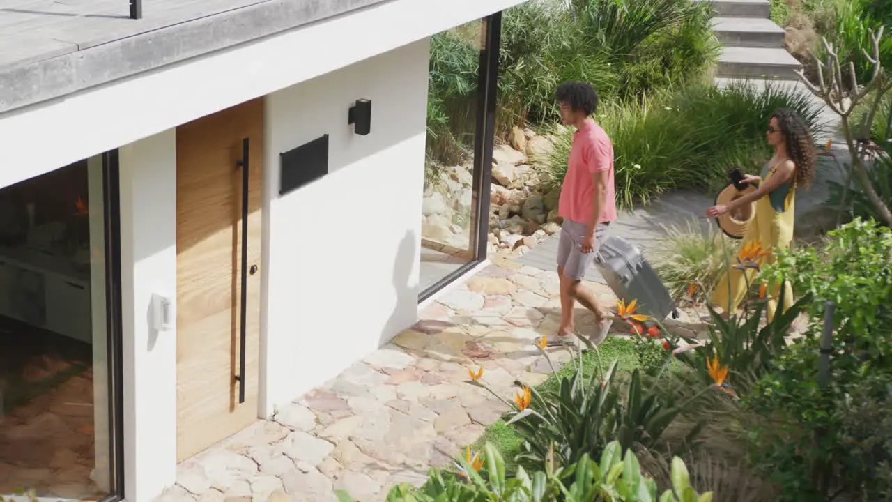 Video of happy diverse couple arriving with suitcase at the door of sunny holiday home