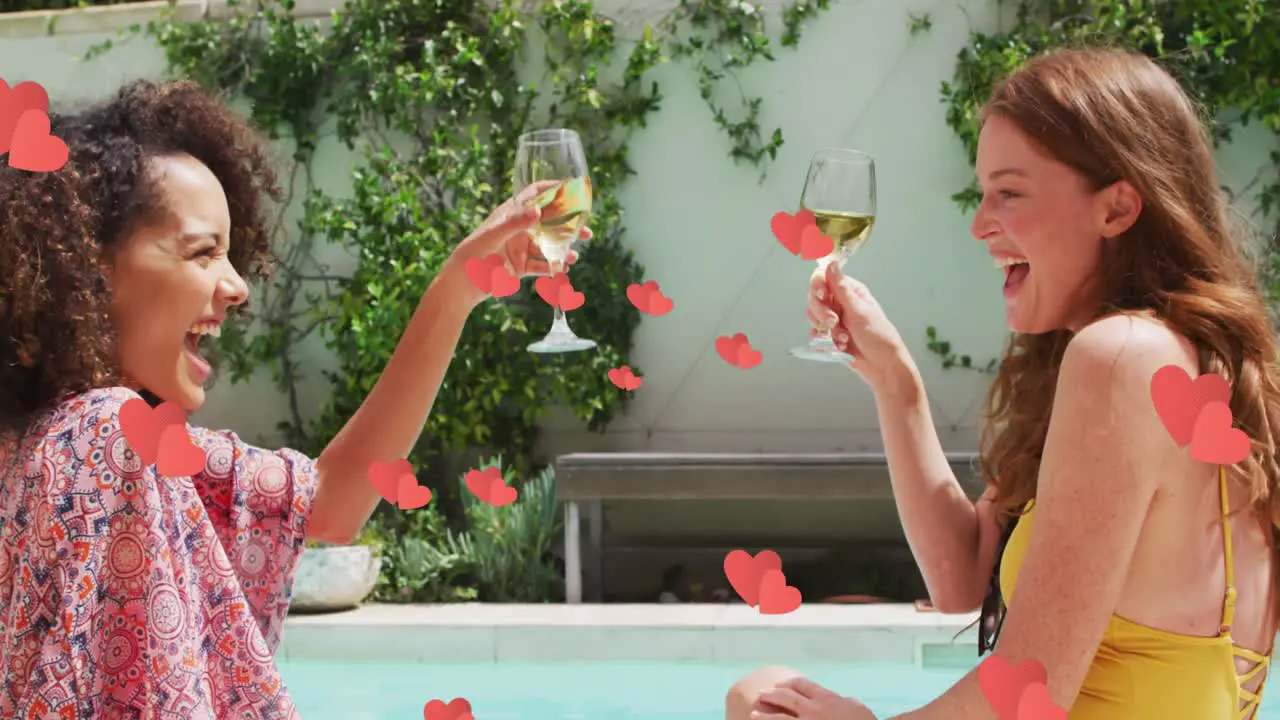 Multiple red hearts floating against two diverse female friends toasting drinks by the pool