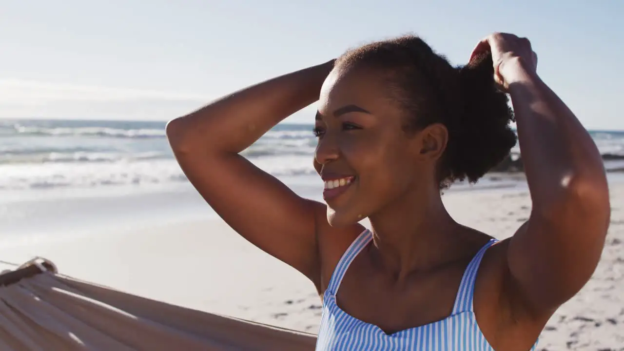 Close up of african american woman smiling while sitting on a hammock at the beach