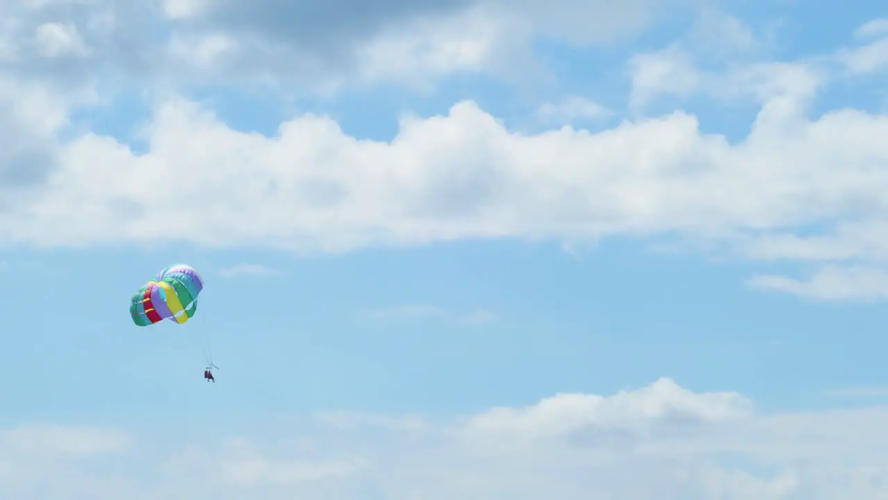 View of couple flying in a parachute pulled by a boat over a blue sky with white clouds