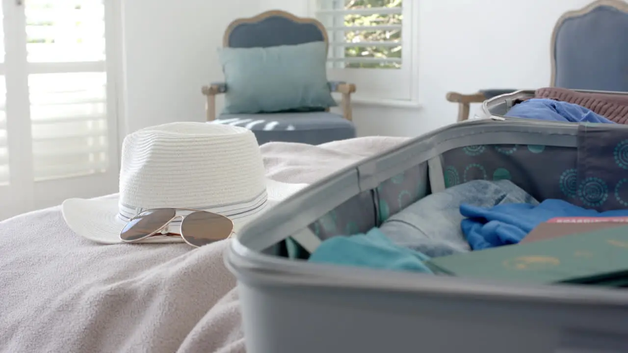 Close up of suitcase hat and sunglasses on bed in bedroom slow motion