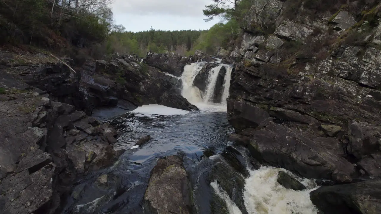 Drone footage flying quickly and low against the stream in the river towards small waterfall Rogie Falls Powerful Waterfall in Scotland