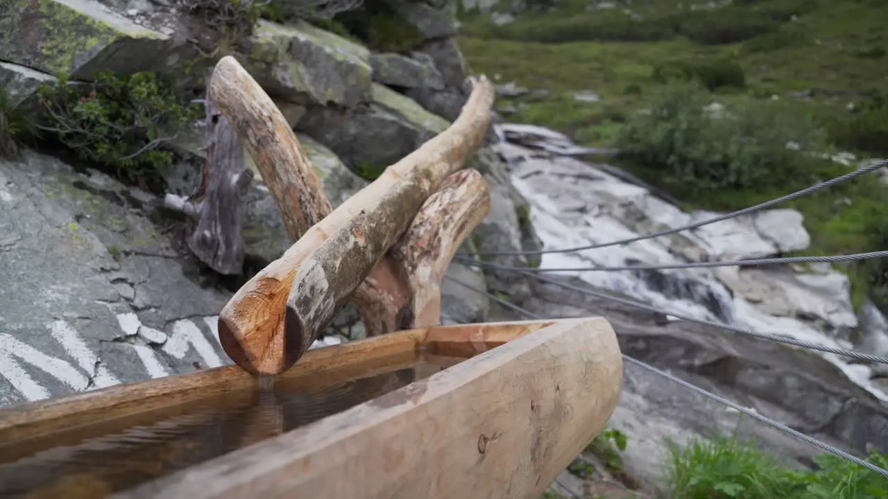 A wooden fountain with drinking water next to a river in the Austrian alps