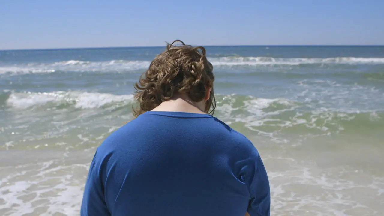 a teen boy gazes out at the ocean and then walks away