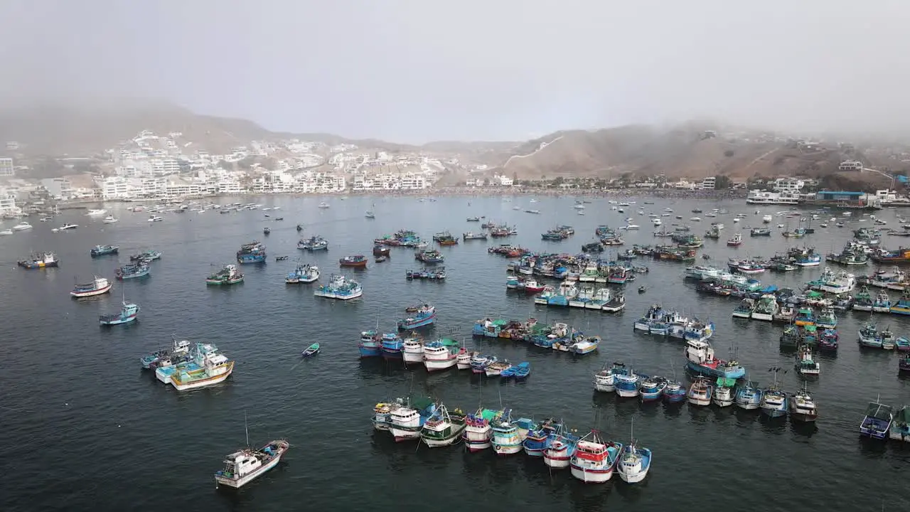 Drone shot of fishing boats in a fishing port next to beach houses and yachts in the cost of Pucusana Peru during summer