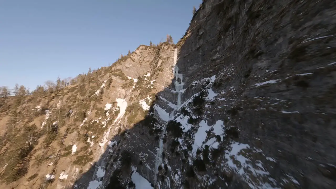 fpv drone flying trough a frozen waterfall in the austrian mountains at sunset