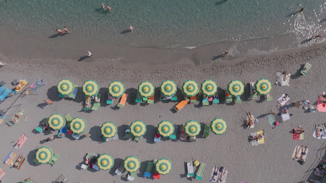 Top down aerial footage of the waves of the sea rolling up to the beach with tourists and beach umbrellas