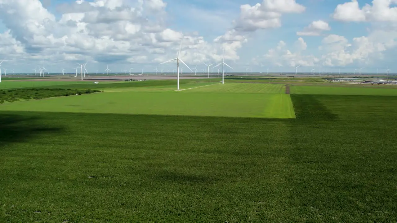 Wide angle drone aerial footage zoom into wind turbines spinning on a clear summer day over a green field in Texas