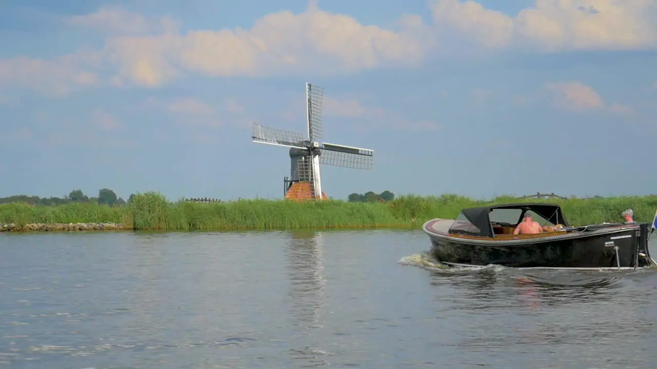 Dutch Old Windmill on a dike near the water a small Dolly shot in slowmotion an other boat is sailing by from right to left