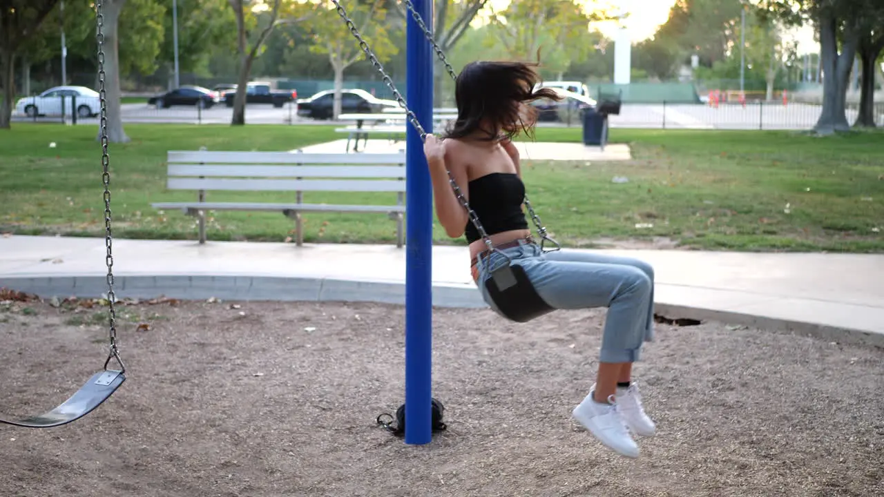 A beautiful hispanic girl playing and having fun on the playground swing set wearing retro pink sunglasses in slow motion