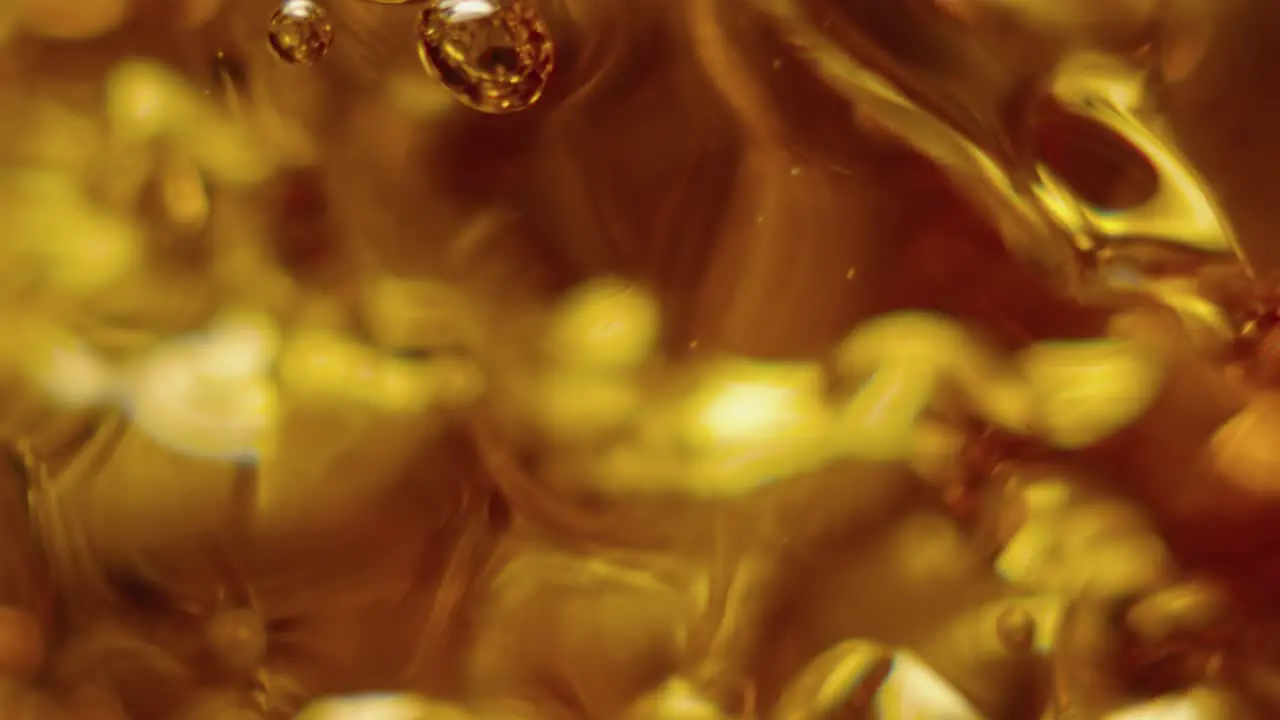 A glass is slowly filling with ambar liquid in slowmotion and macro