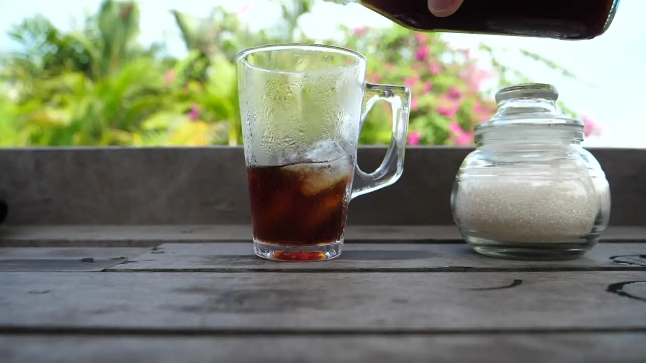 Close-up of person refilling their iced beverage on outdoor patio with tropical background