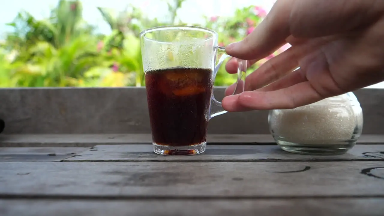 Hand grabbing an iced beverage to take a drink with a tropical background