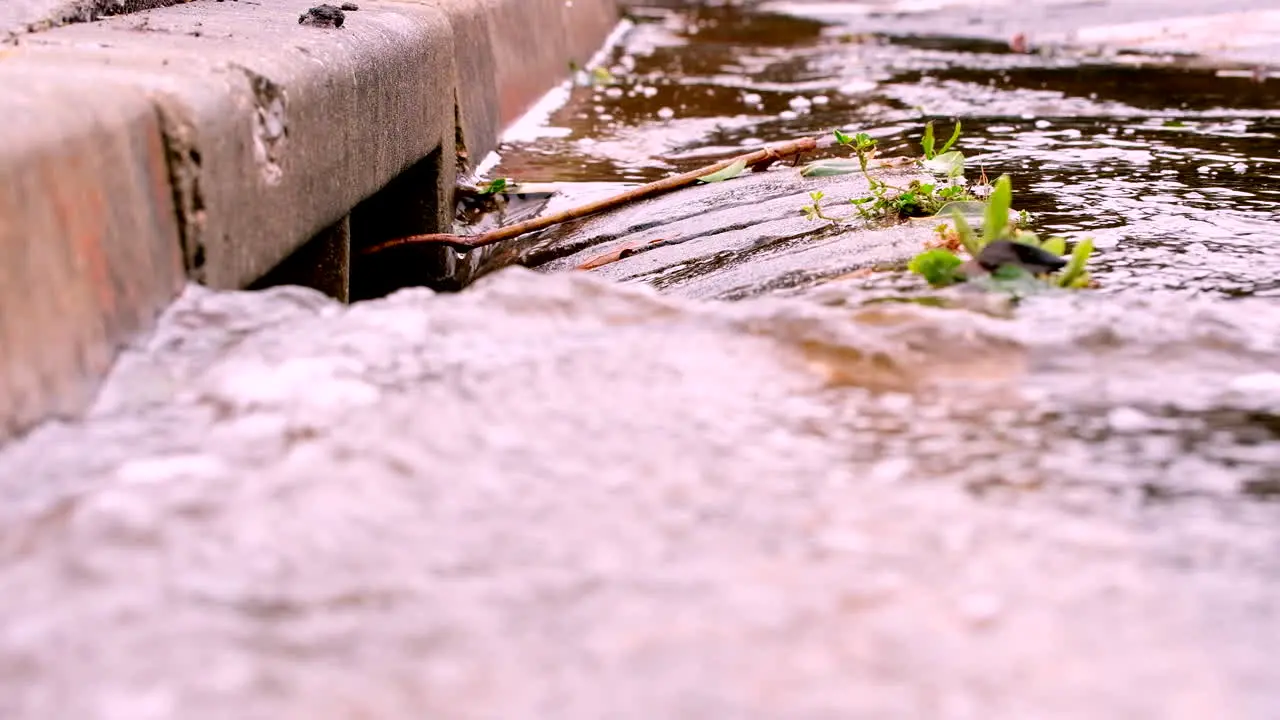 Closeup of rainwater runoff flowing down concrete gutter into street drain