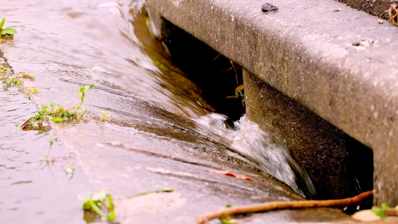 Rainwater runs down concrete gutter into road drain global warming concept