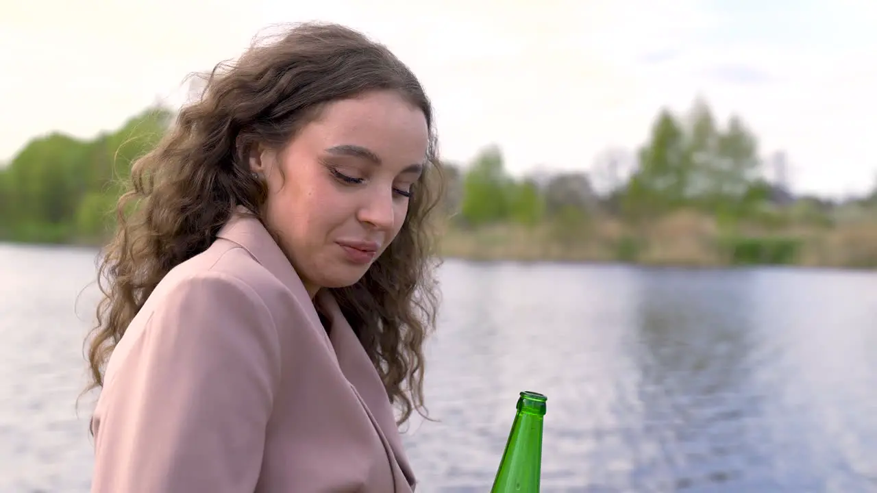 Happy Curly Brunette Woman Talking With Her Friend And Drinking Beer On The Riverside