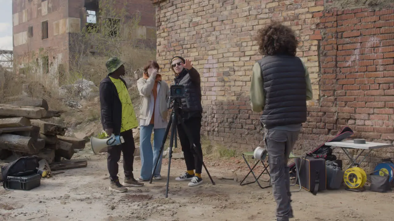 Three Production Coworkers Talking About A Recording Project In Front Of A Camera On A Tripod In The Street While Another Worker Taking Notes