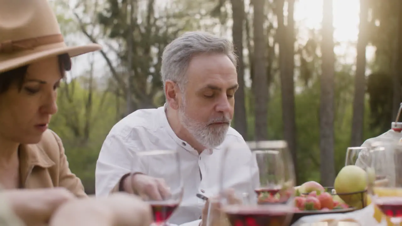 Middle Aged Man Eating And Talking To His Friends Sitting At Table During An Outdoor Party In The Park