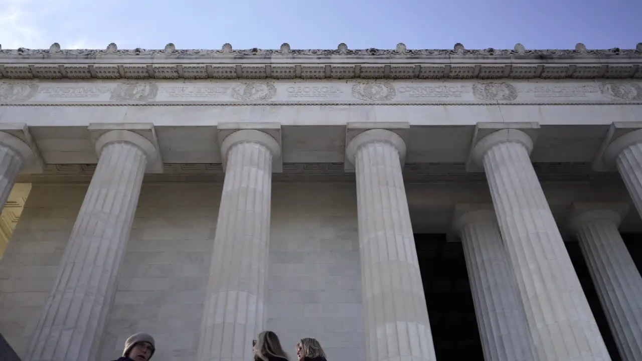 Tourists on Lincoln Memorial Low angle panning through Columns against blue sky