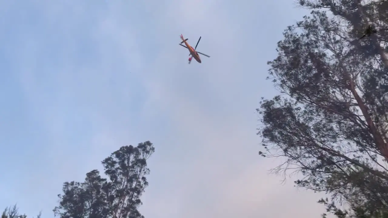 An amphibious helicopter carrying water on its monsoon bucket rushes to throw water on a wildfire that is consuming the area