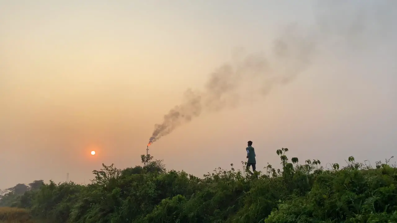 Wide establisher static shot of man running in rural road by polluting industry