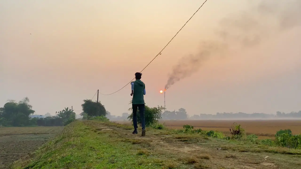 Running man jogging in countryside polluted area burning gas plant behind