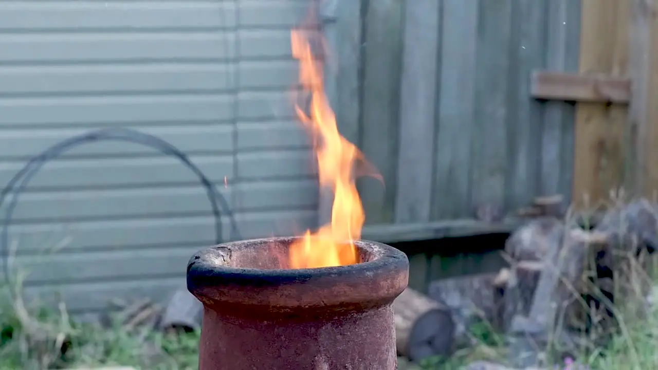 Flames lick up out the top of a terra-cotta chimenea during late evening